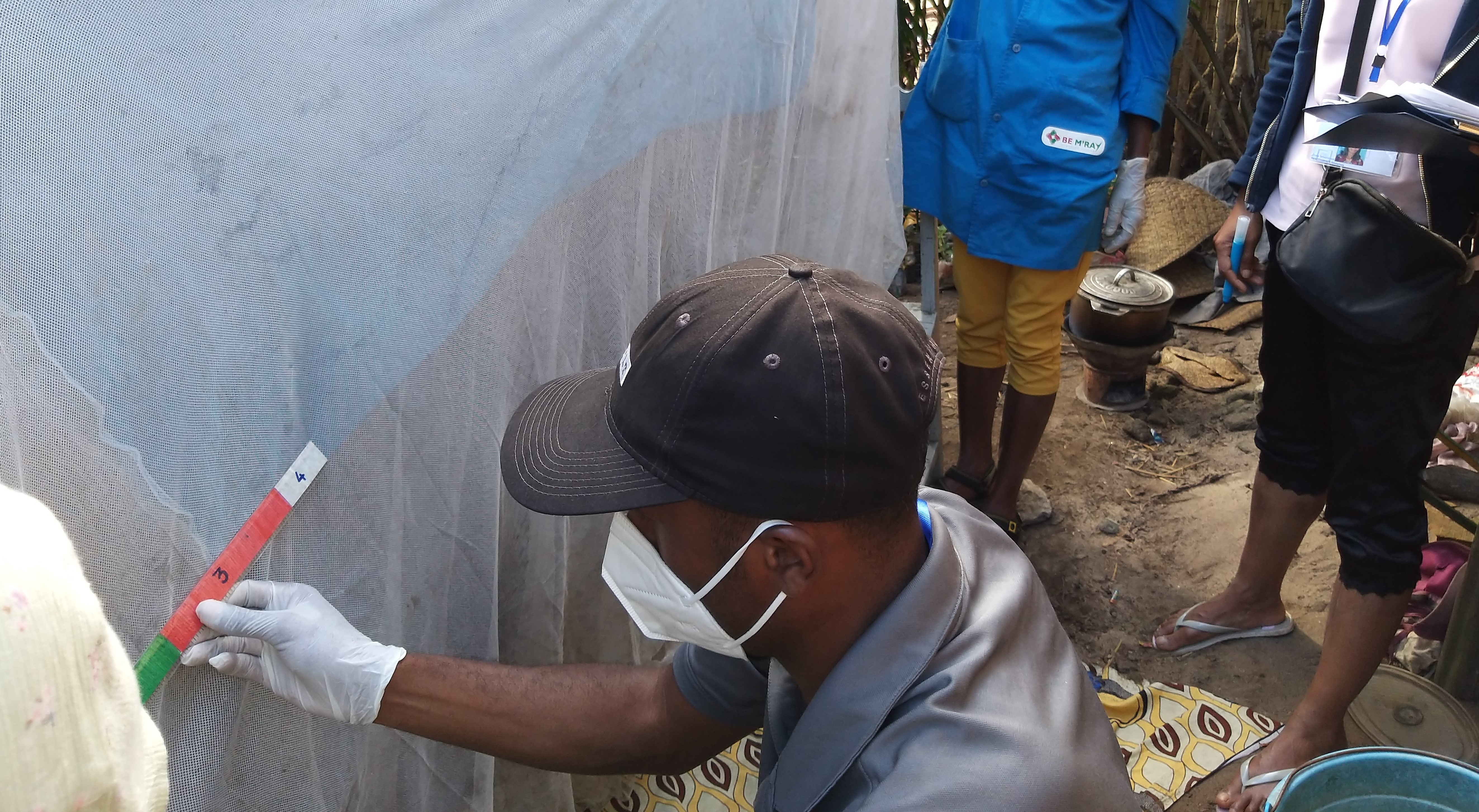 A community health worker in Madagascar’s Toamasina II district holds an ITN while the durability monitoring team identifies and counts holes in the net.