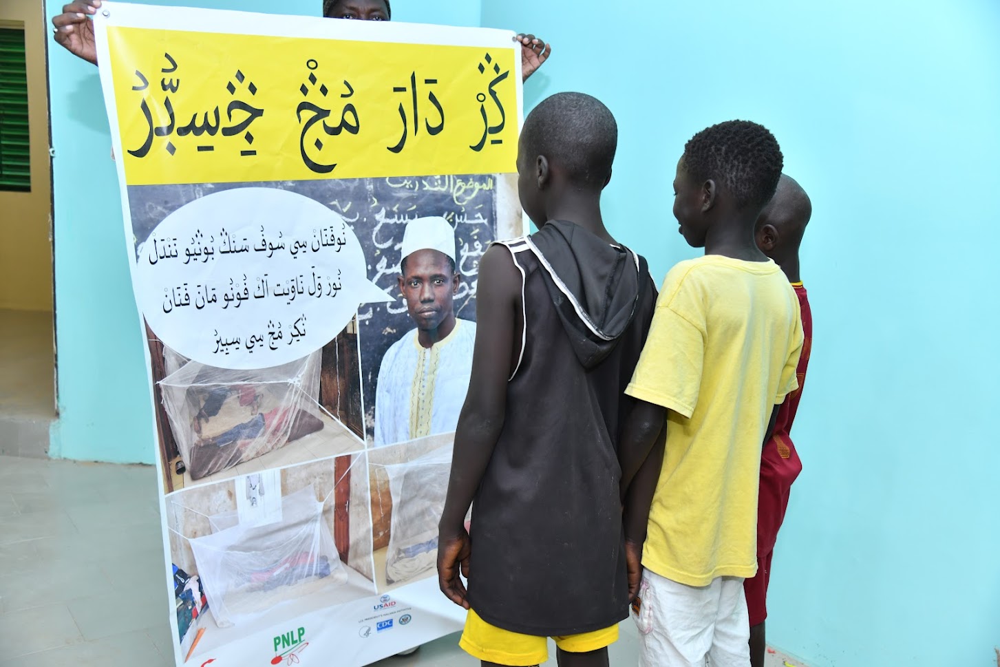 Talibé children in front of the poster in Wolof written in Arabic.