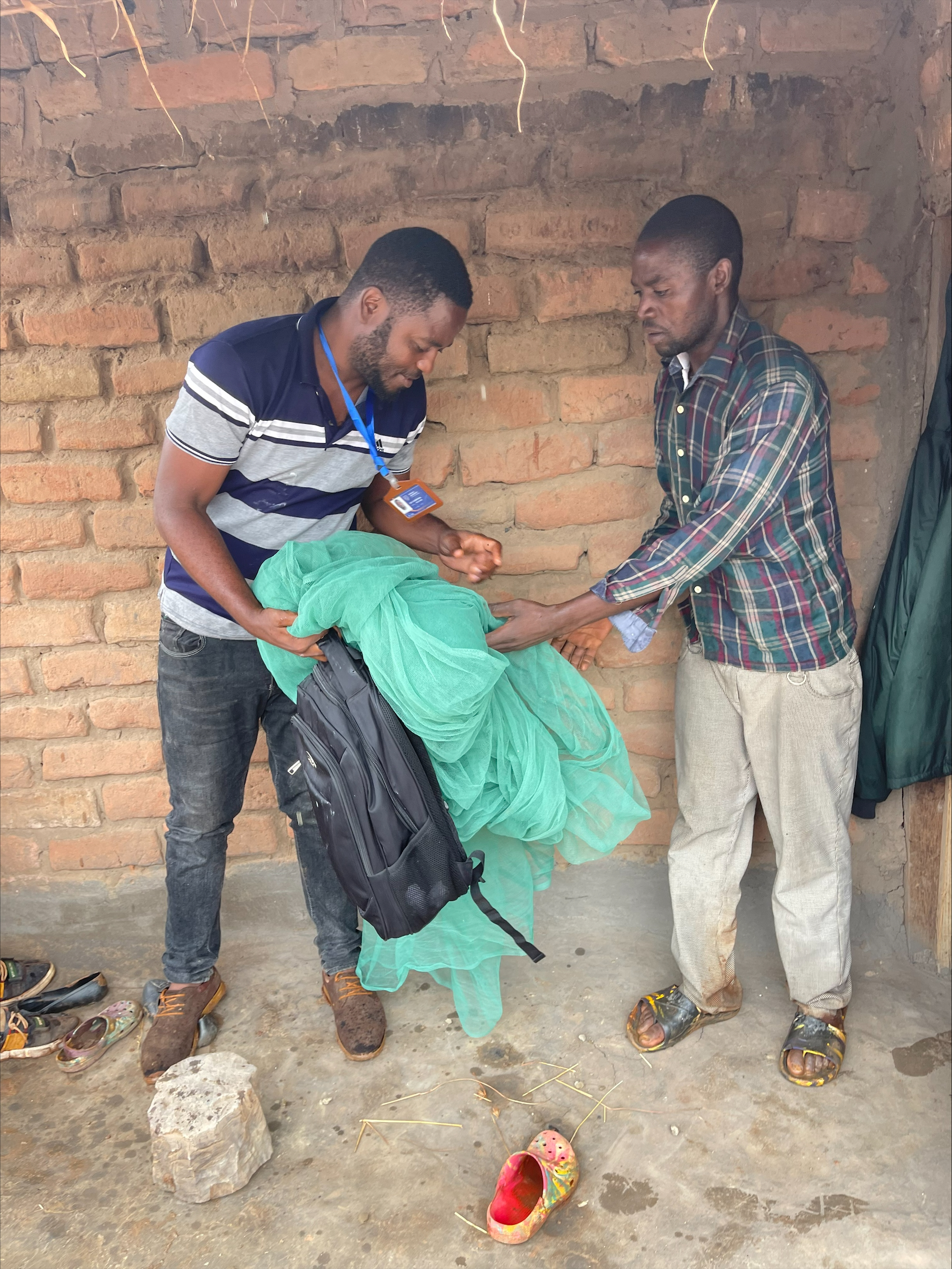Two men holding a green mosquito bed net, conducting 12-month ITN durability monitoring of new ITNs.